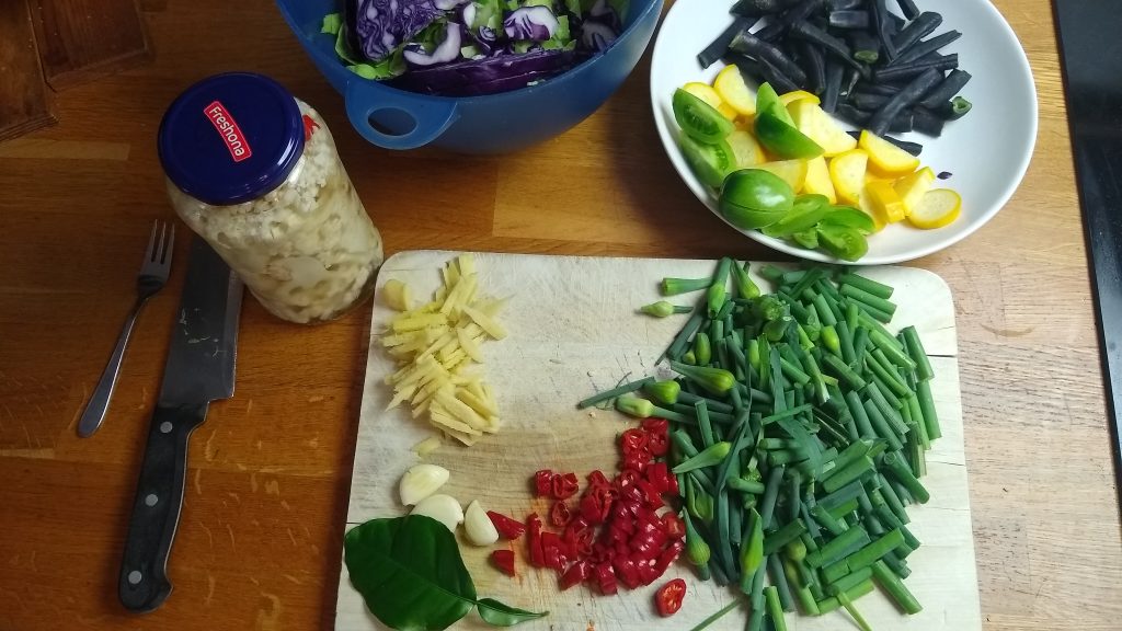 Küchenarbeitsfläche mit Holzbrett, Kochmesser, klein geschnittenem Gemüse und Gewürzen