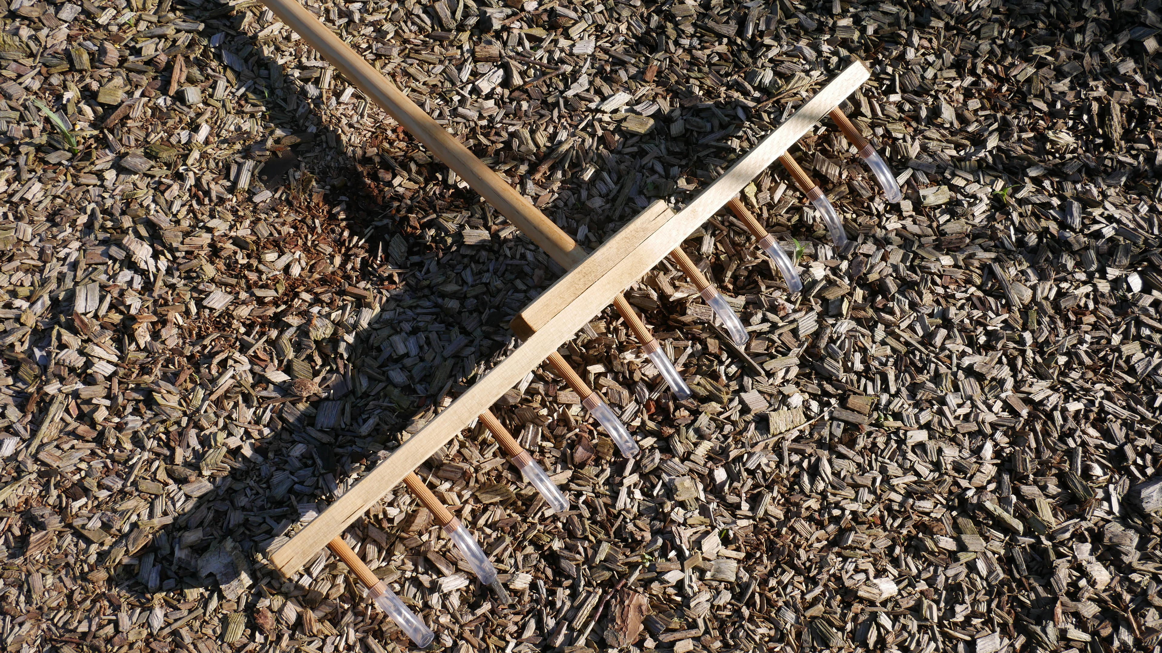 wooden rake with pieces of hose on the pins for marking drills in garden beds.
