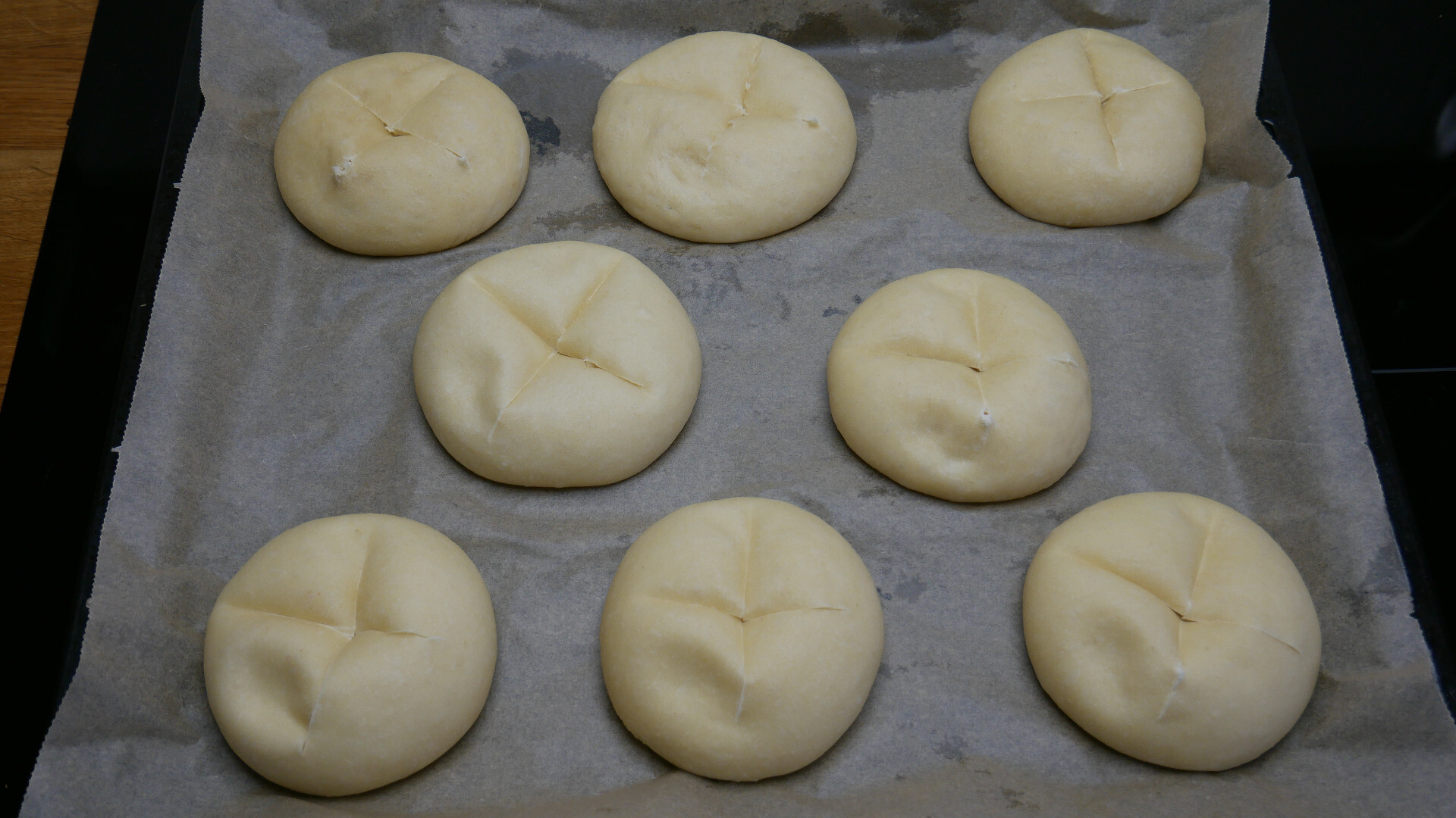 Discs and balls of yeast dough on a baking tray after proving with incisions 
